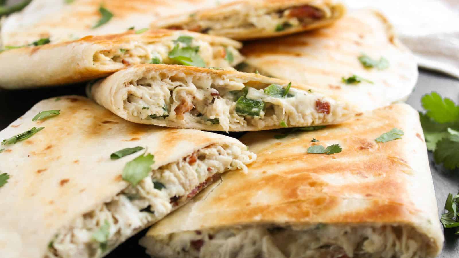 Close-up of folded tortillas filled with chicken, cheese, and herbs, garnished with cilantro.