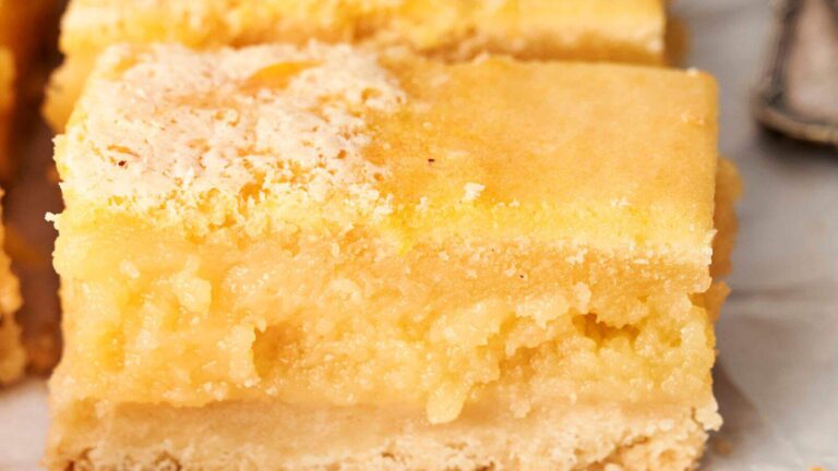 Close-up of two stacked lemon bars, showing a crumbly crust and a thick, creamy lemon filling with a lightly powdered top.