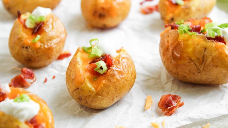 Baked baby potatoes topped with melted cheese, sour cream, bacon bits, and chopped green onions on parchment paper.