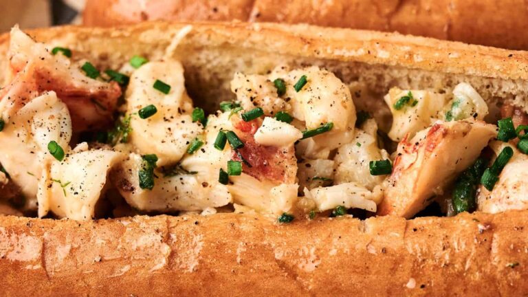 Close-up of a lobster roll with chunks of lobster meat, chopped chives, black pepper, and a toasted split-top bun.