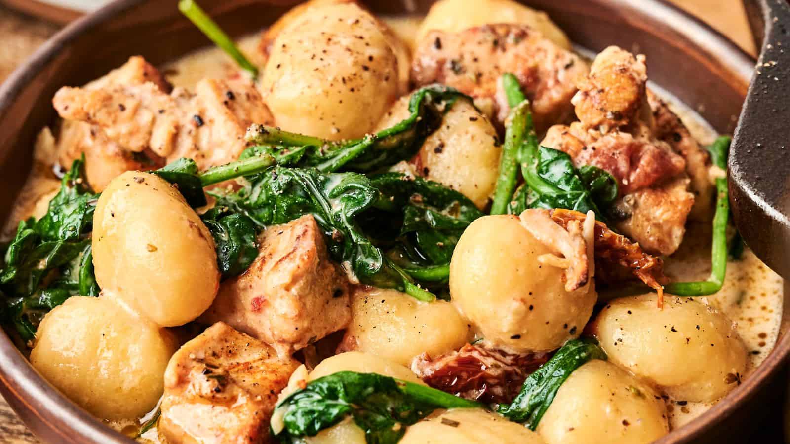 A bowl of gnocchi with pieces of chicken, wilted spinach, and a creamy sauce, garnished with black pepper.