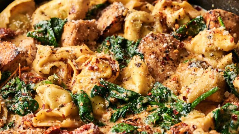 Creamy tortellini pasta with spinach, grilled chicken slices, and a sprinkle of grated cheese and herbs.