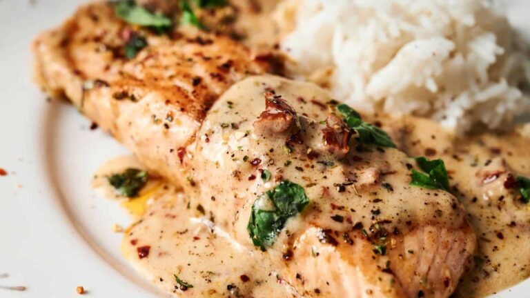 Grilled salmon fillet topped with creamy herb sauce, garnished with chopped cilantro, served with a side of white rice.