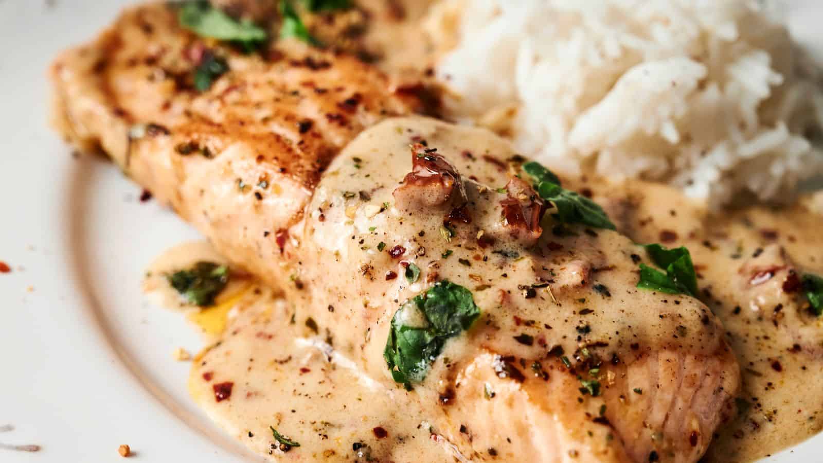 Grilled salmon fillet topped with a creamy herb sauce, served next to a portion of white rice.