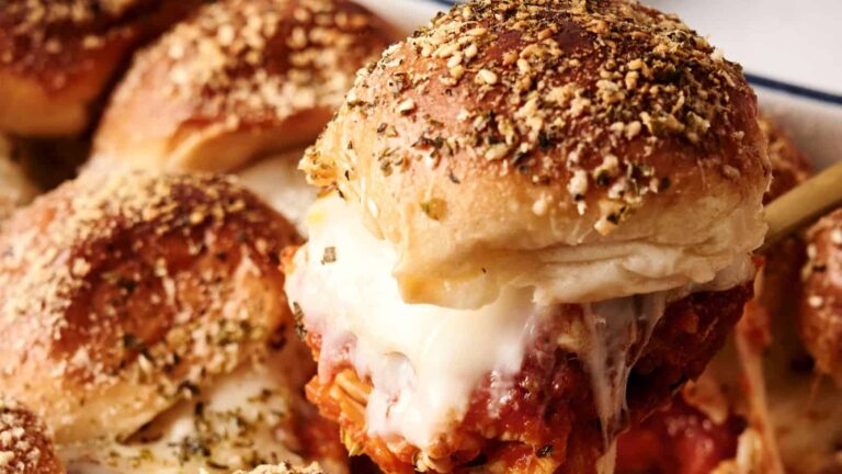 A close-up of a baked sandwich filled with chicken, marinara sauce, and melted cheese, topped with herbs and grated cheese.