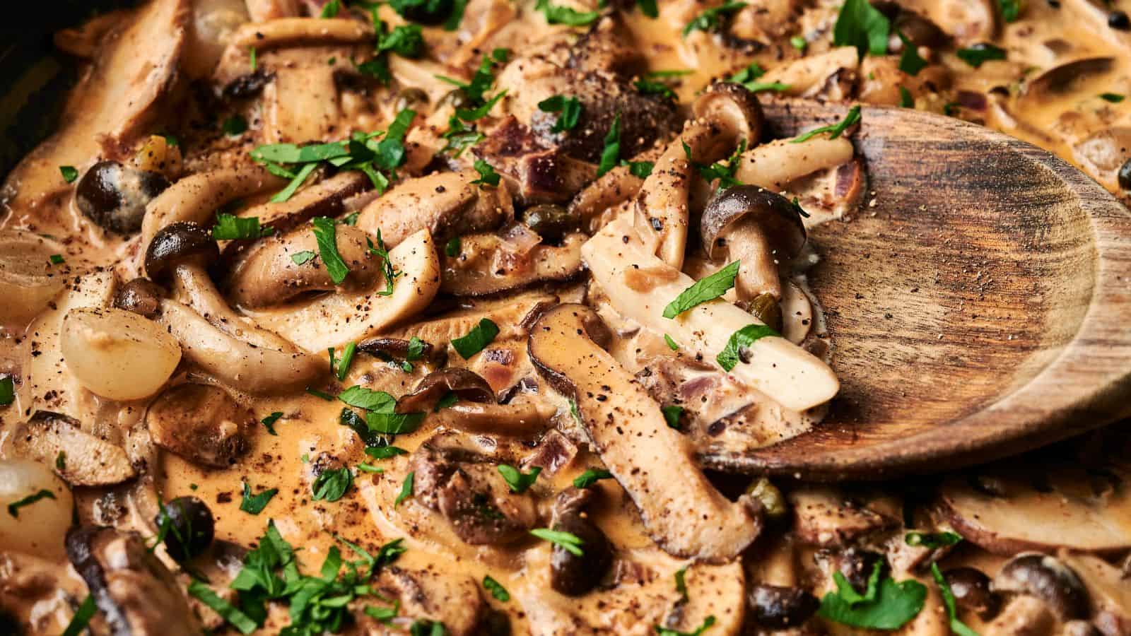 Creamy mushroom sauce with herbs and sliced mushrooms, stirred with a wooden spoon.