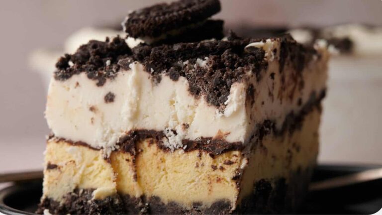 A slice of layered ice cream cake with chocolate cookie crumbles and a cookie on top, served on a plate.