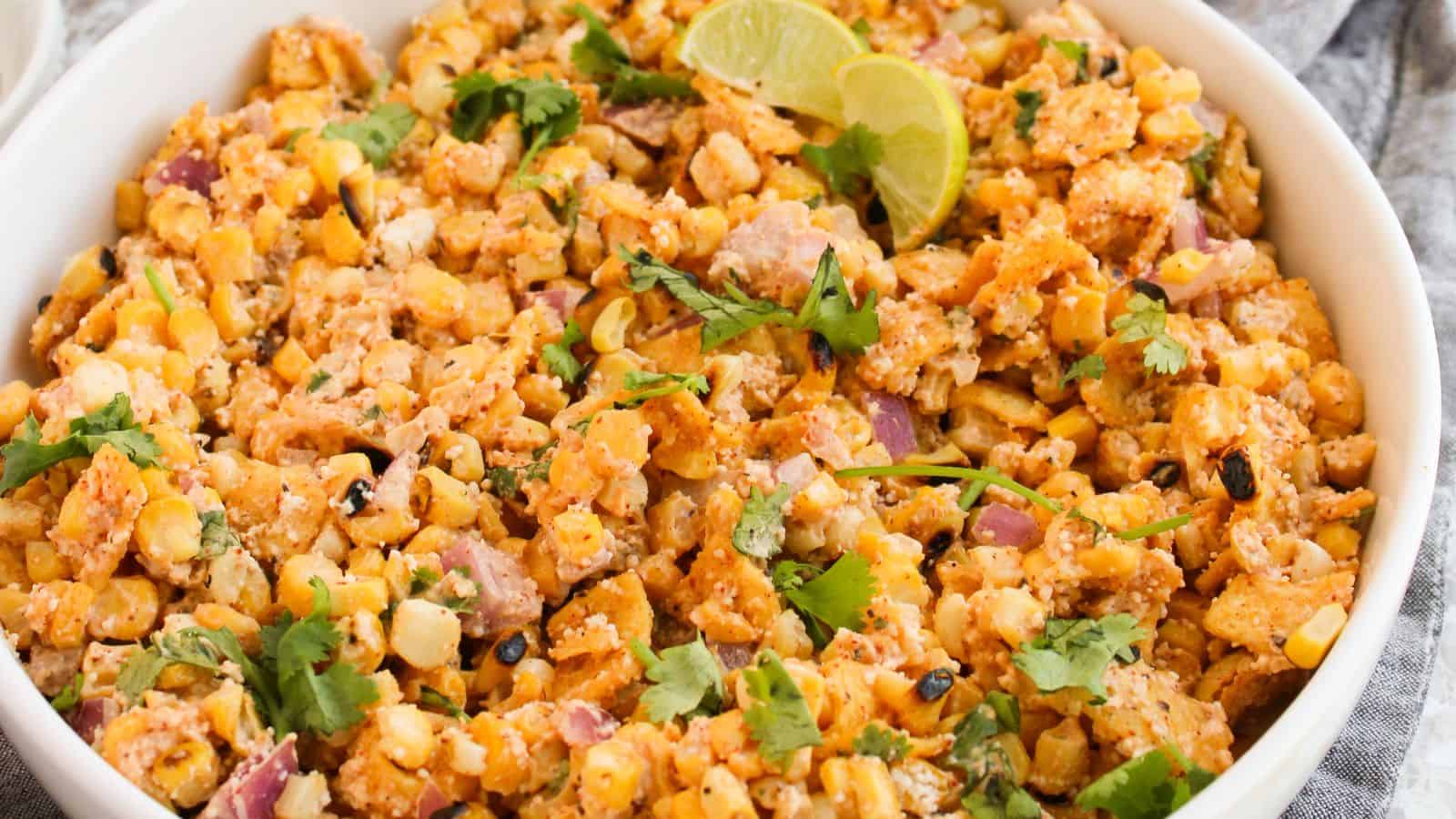 A bowl of Mexican street corn salad garnished with lime wedges and cilantro.