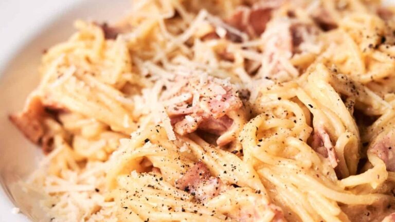 Close-up of spaghetti carbonara topped with grated cheese, pieces of bacon, and a sprinkle of black pepper.