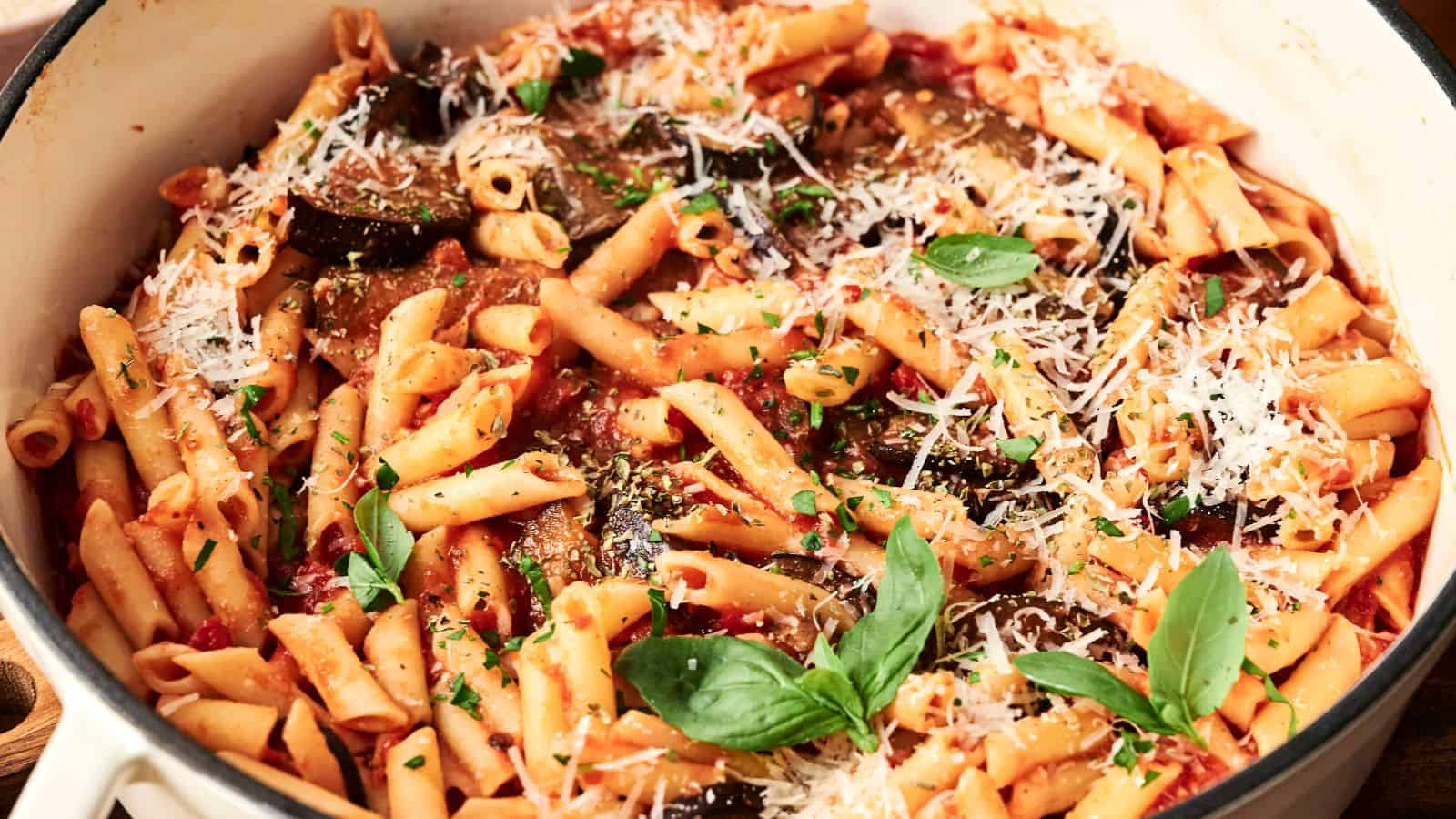 A pot filled with penne pasta in a tomato sauce, topped with grated cheese, basil leaves, and herbs.