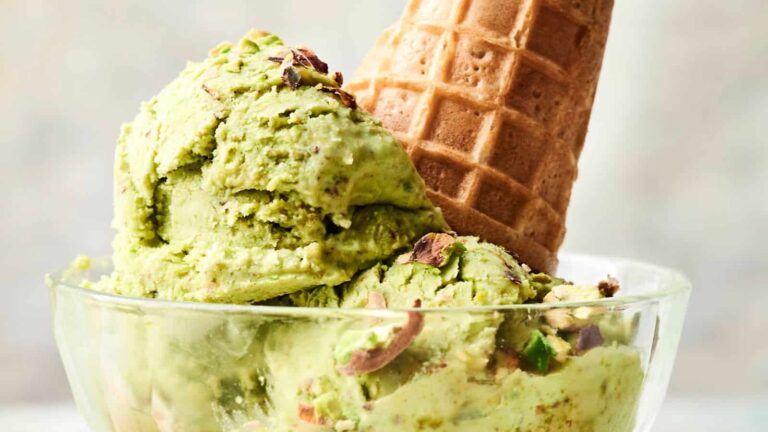 A glass bowl with scoops of pistachio ice cream, garnished with chopped pistachios and a waffle cone.