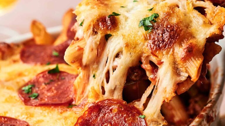 A close-up of baked pasta with melted cheese, pepperoni slices, and sprinkled parsley being served from a dish.