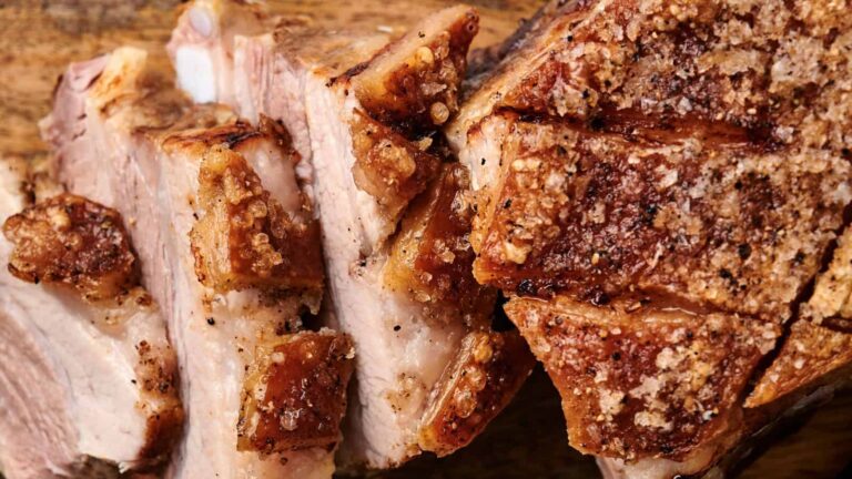 Close-up of sliced roast pork with crispy, seasoned skin on a wooden surface.