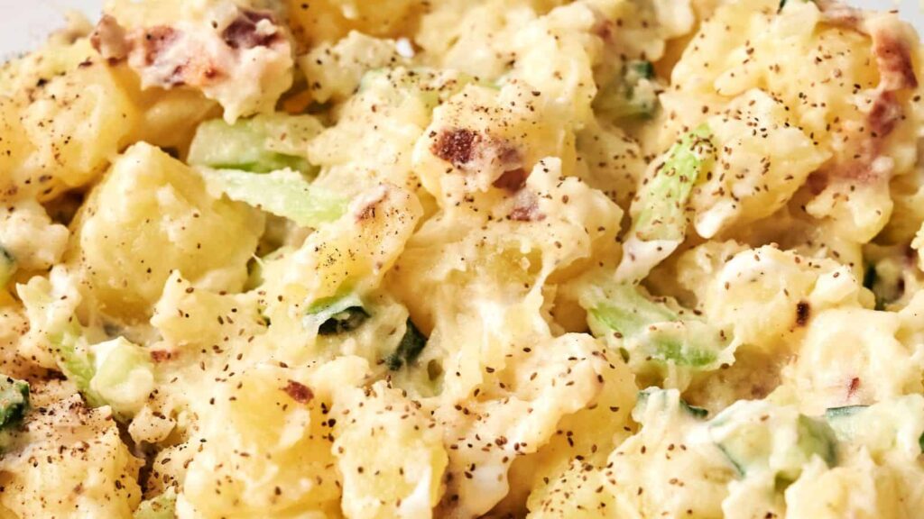 Close-up of creamy potato salad with chunks of potato, celery slices, and sprinkled black pepper.