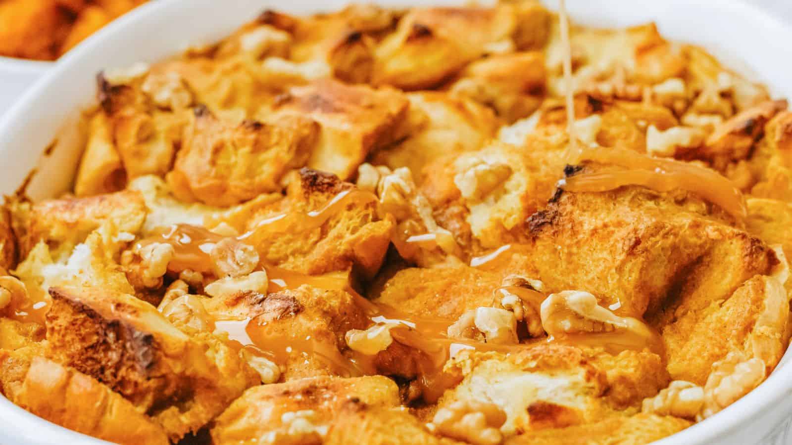 Close-up of a dish of bread pudding with walnuts drizzled with caramel sauce in a white baking dish.