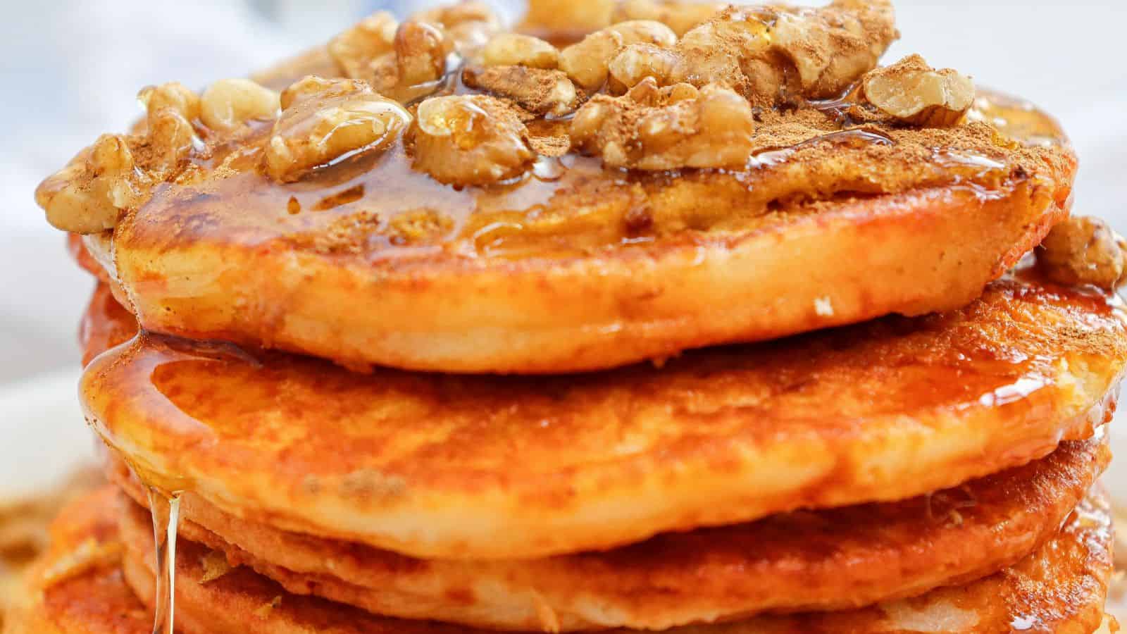 Close-up of a stack of pancakes topped with walnuts and drizzled with syrup.