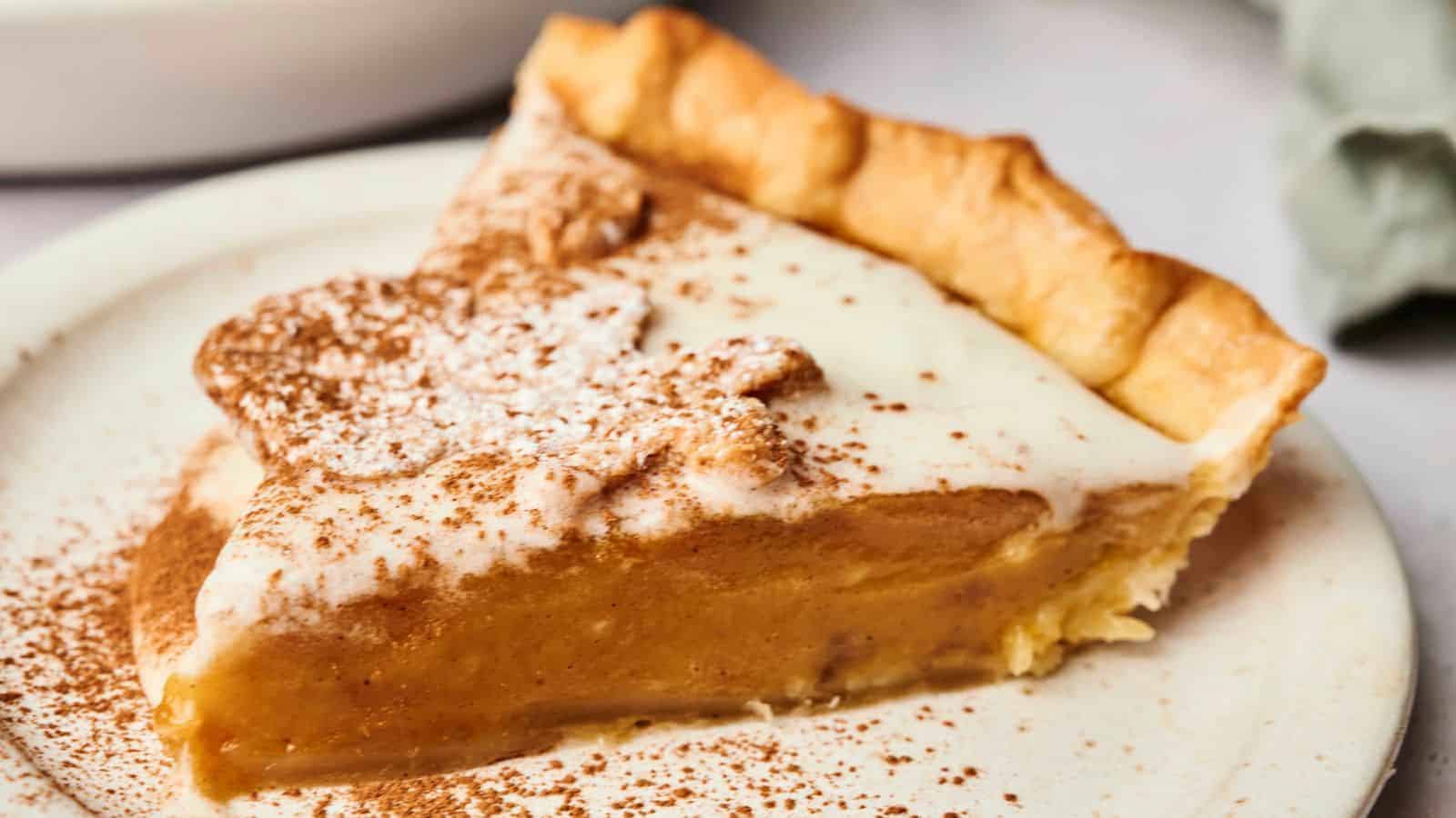 A slice of vegan spiced pumpkin pie topped with whipped cream and a light dusting of cinnamon on a white plate.