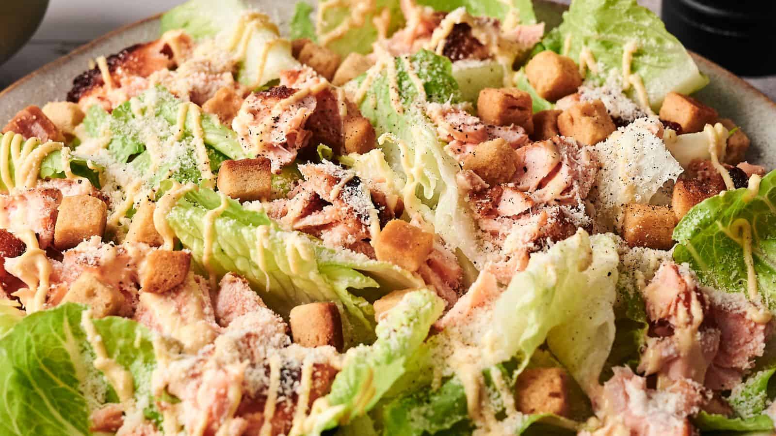 Close-up of a Caesar salad with romaine lettuce, croutons, shredded chicken, grated cheese, and a creamy dressing.