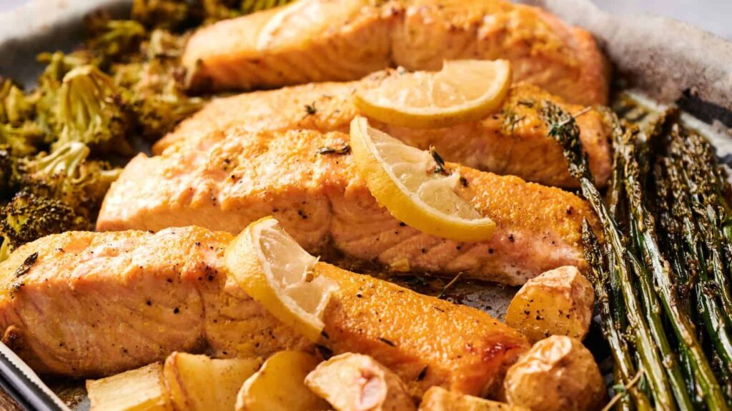 Baked salmon fillets topped with lemon slices, served with roasted broccoli, asparagus, and potatoes.