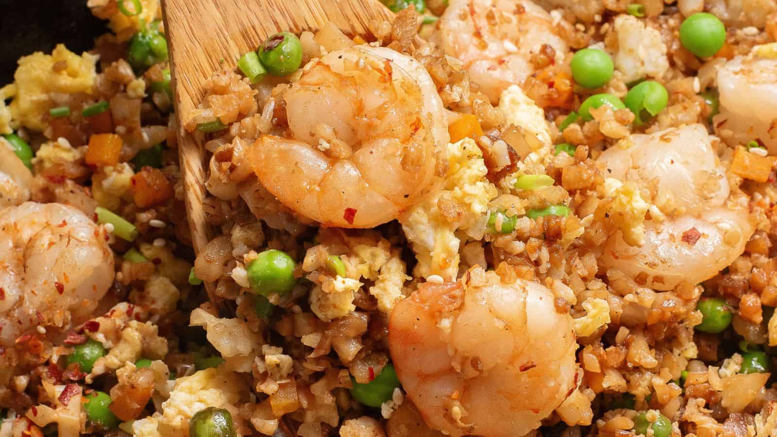 Shrimp fried rice with peas, eggs, and diced vegetables being stirred with a wooden spatula.