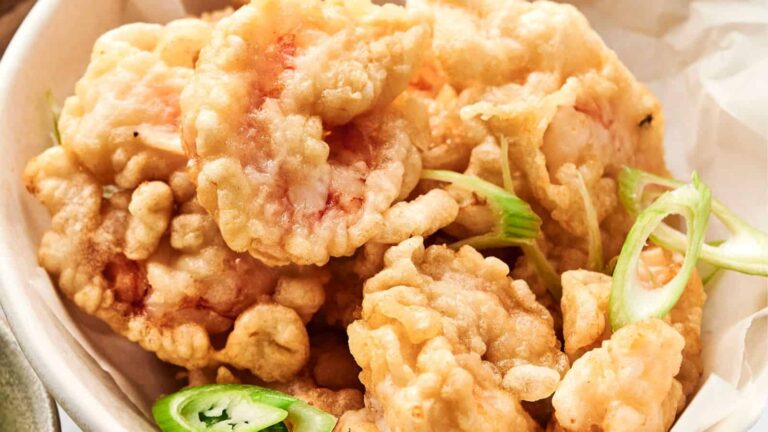 A bowl of golden-brown tempura shrimp garnished with slices of green chili and scallion.