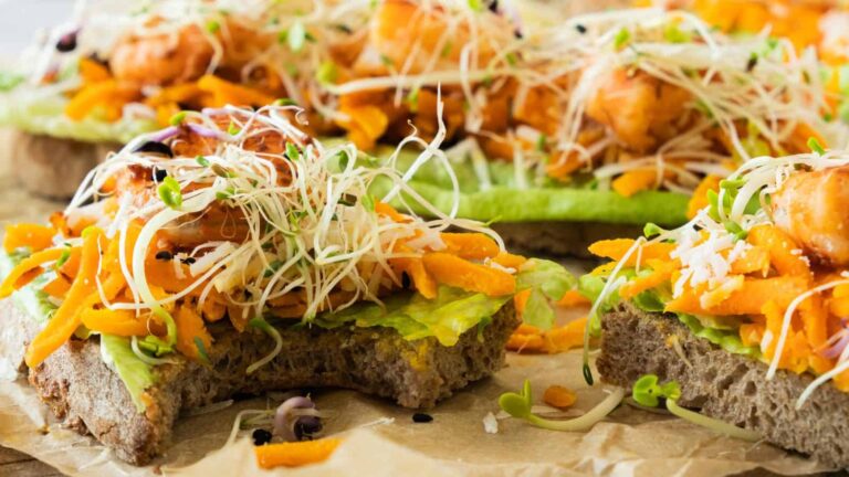 Open-faced sandwiches on whole grain bread topped with avocado, grated carrots, sprouts, and pieces of cooked chicken.