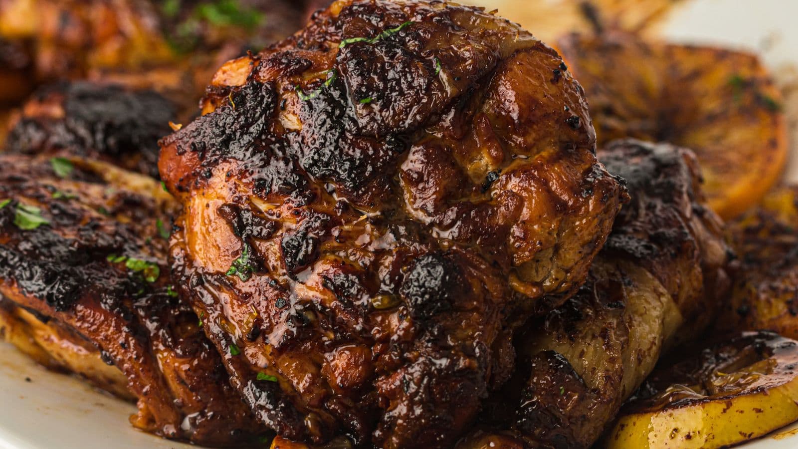 Close-up of grilled, well-seasoned, and charred chicken pieces with visible herbs on a plate.