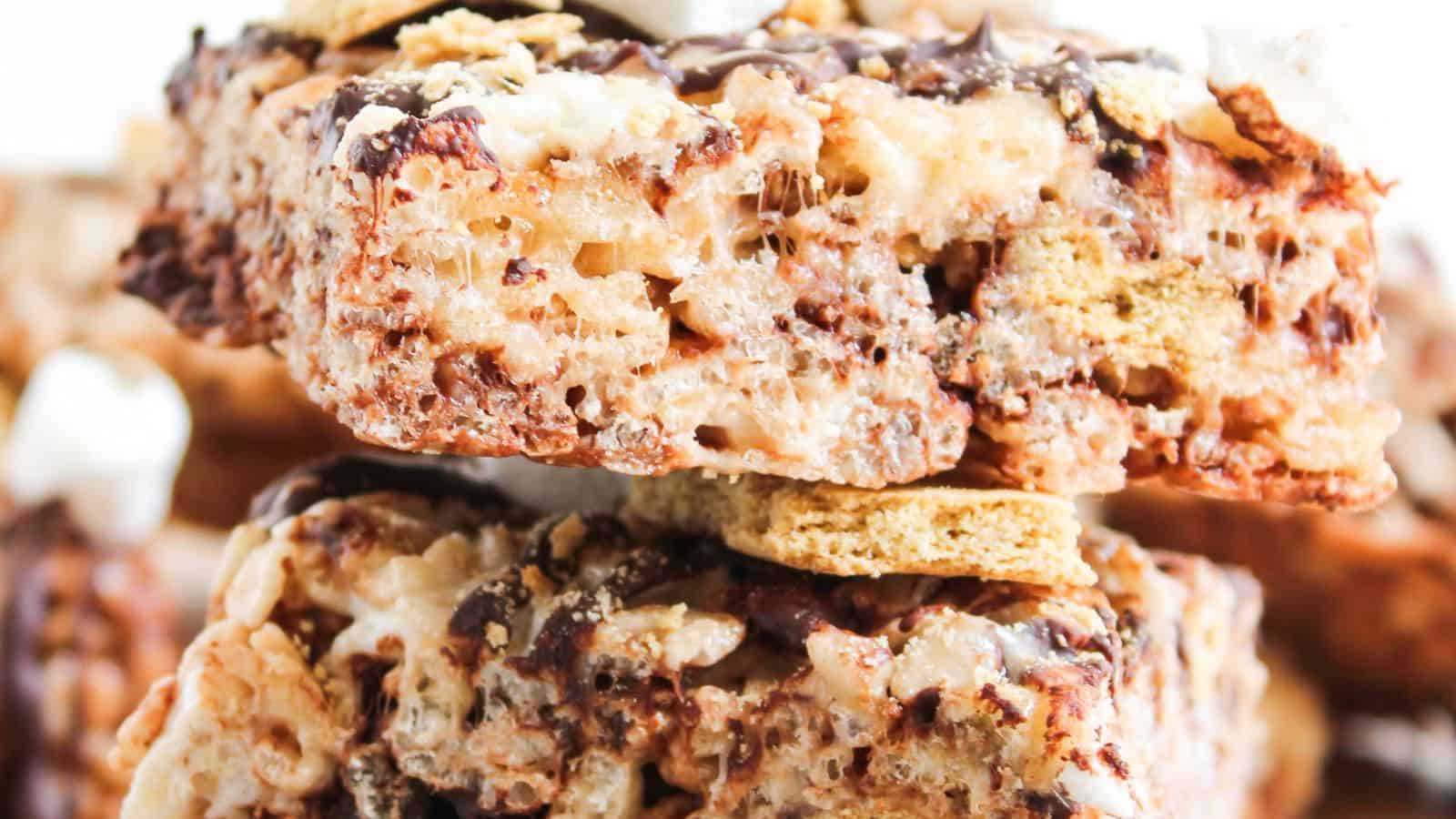 Close-up of stacked dessert bars made with crispy rice cereal, marshmallows, graham cracker pieces, and chocolate drizzle.