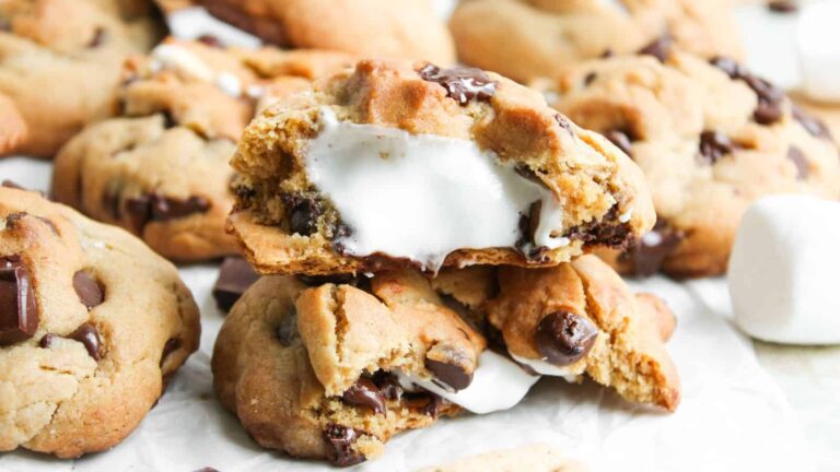 A close-up of chocolate chip cookies filled with melted marshmallow, with one cookie broken open to show the gooey center.