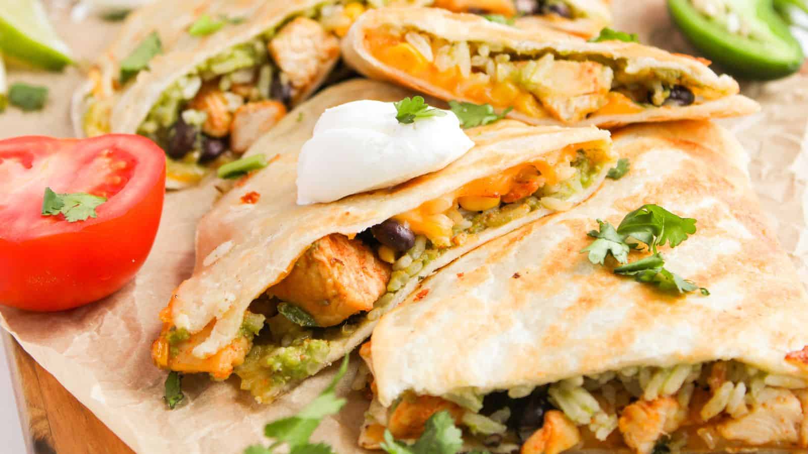 Quesadillas filled with rice, beans, and chicken, topped with sour cream and cilantro. Sliced tomato and jalape&ntilde;o are on the side.