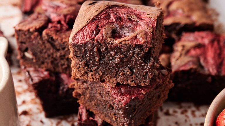 Close-up of two chocolate brownies with a swirled topping of what appears to be raspberry puree, showing a dense and moist texture.