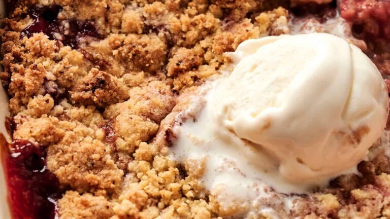 A close-up of fruit crumble topped with a scoop of melting vanilla ice cream.