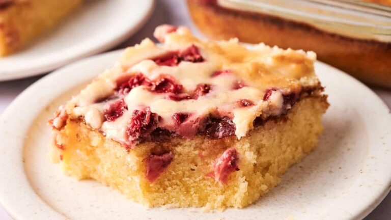 A square slice of cherry-topped cake with a creamy layer, served on a white plate.