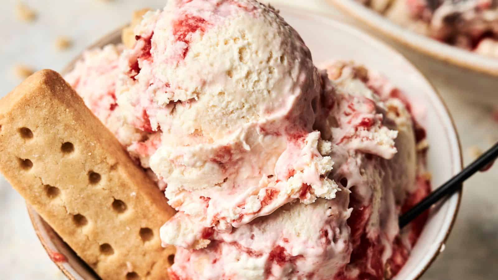 A bowl of strawberry swirl ice cream topped with a rectangular shortbread biscuit, with a spoon on the side.