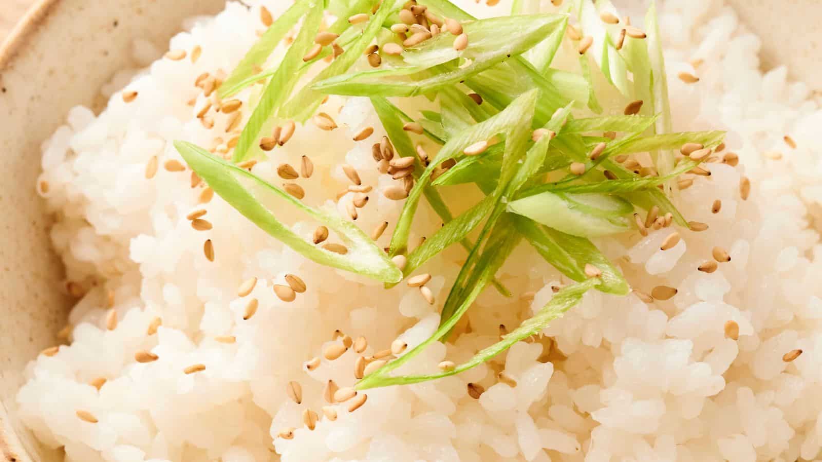 A bowl of steamed white rice topped with sliced green onions and sprinkled with sesame seeds.