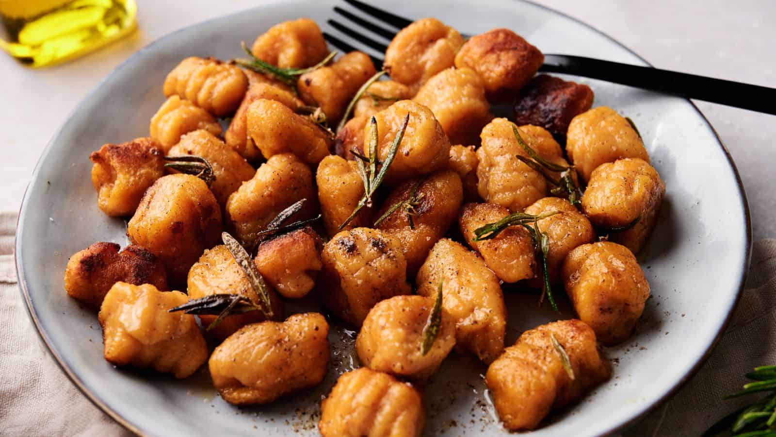 A plate of golden-brown gnocchi garnished with rosemary, served with a black fork.
