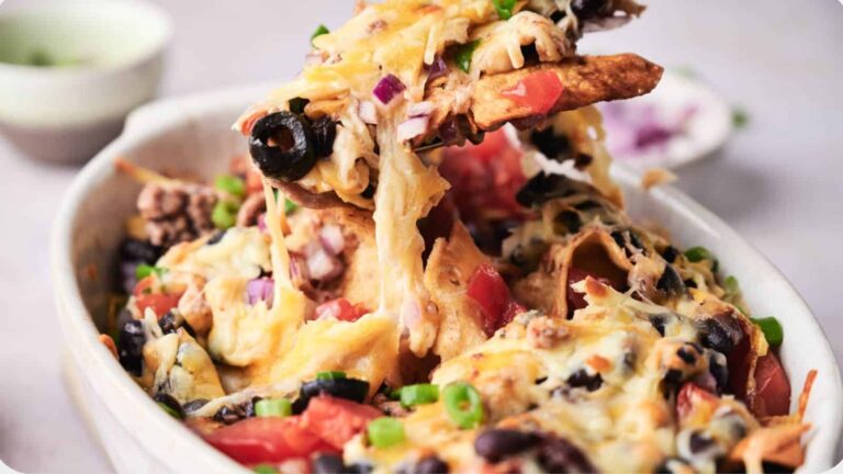 A close-up of cheesy nachos topped with black olives, tomatoes, ground beef, onions, and green onions in a white dish.