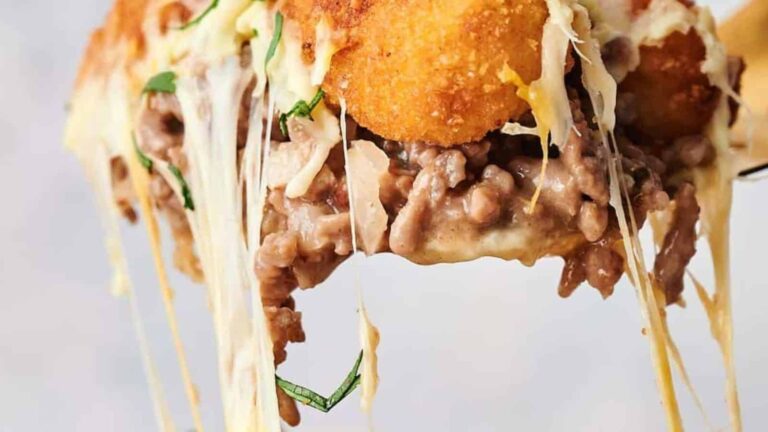 Close-up of melted cheese, minced meat, herbs, and a breaded, fried topping, with cheese stretching as the food is lifted.