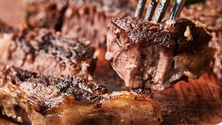 Close-up of a juicy, grilled steak cut into pieces, with one piece being held up by a fork.