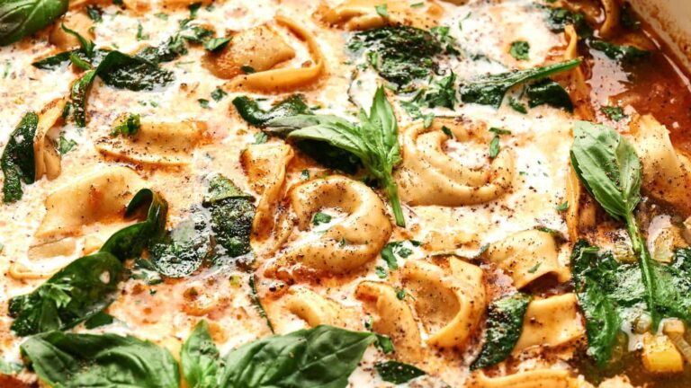 Cheese tortellini in a creamy tomato sauce with spinach and fresh basil leaves, topped with ground black pepper.