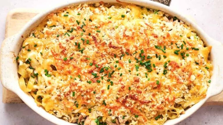 Baked casserole dish filled with pasta, topped with a golden breadcrumb and cheese crust, and garnished with chopped chives.