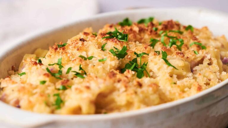 A baked macaroni and cheese casserole topped with golden breadcrumbs and chopped parsley in a white dish.