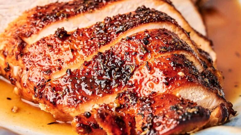 Close-up of sliced, roasted meat with a seasoned, caramelized crust and visible juices on a plate.