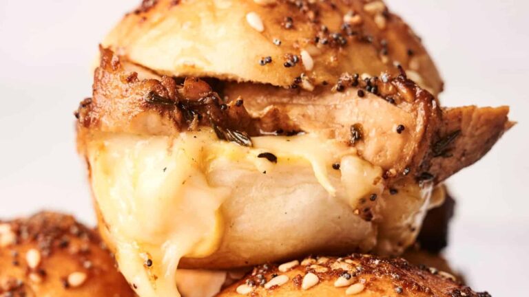 Close-up of a stuffed bread roll with melted cheese and seasoned chicken filling, topped with sesame and poppy seeds.