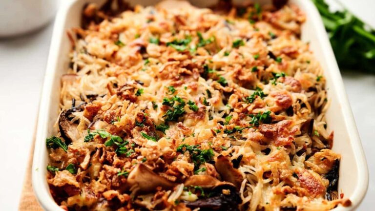 A baked casserole topped with crispy fried onions and chopped parsley in a white rectangular dish.