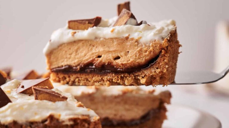 A slice of pie with a crumbly crust, chocolate layer, creamy peanut butter filling, whipped topping, and chocolate pieces on top.