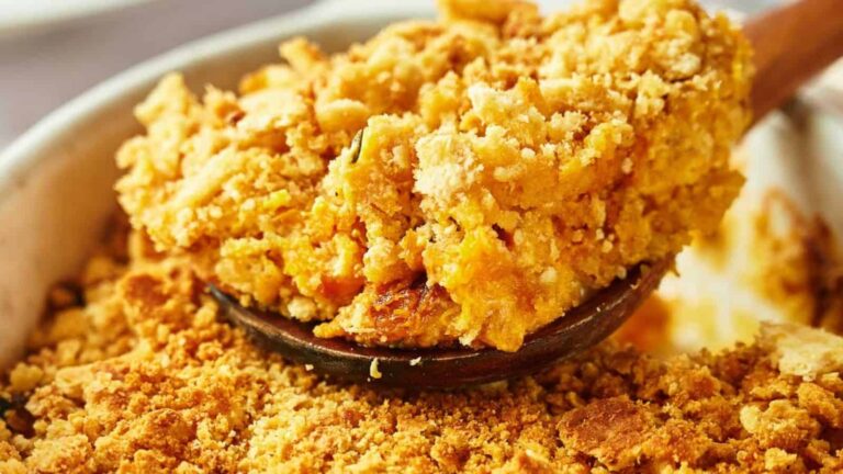 A close-up of a serving spoon holding a portion of golden, crumbly casserole topping, with more casserole visible in the dish below.