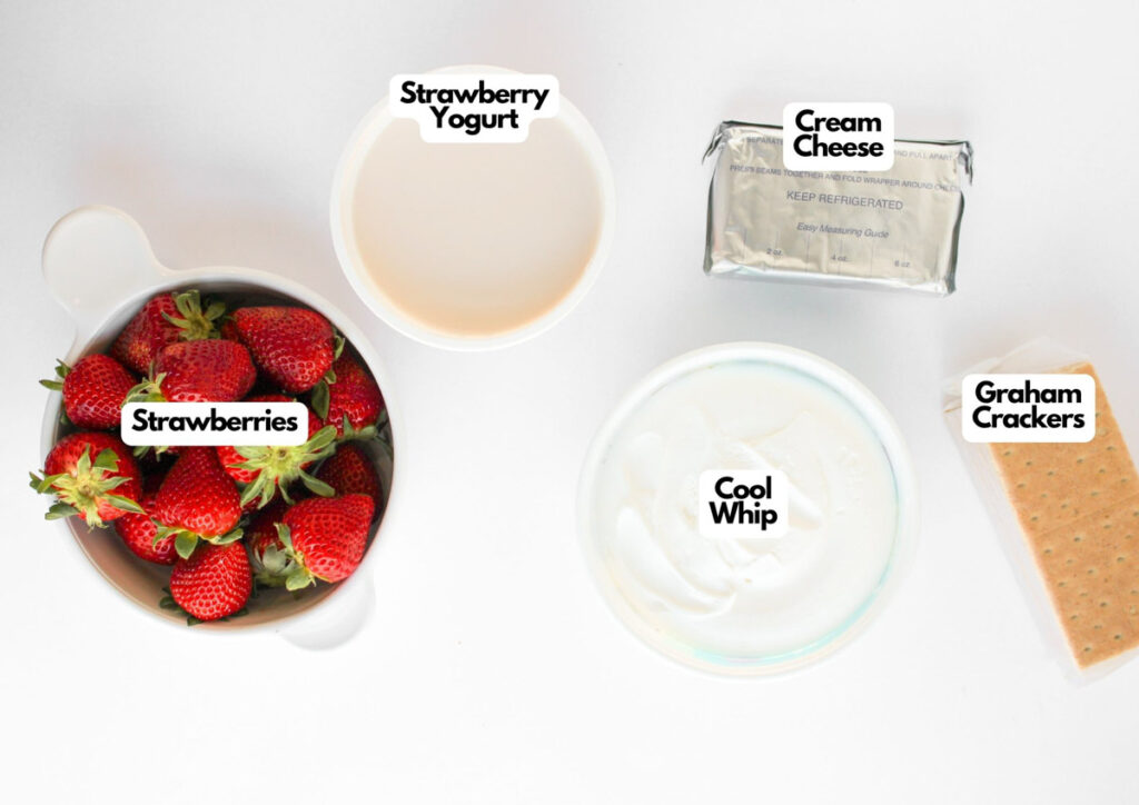 A bowl of strawberries, a cup of strawberry yogurt, cream cheese, Cool Whip, and graham crackers are arranged on a white surface&mdash;everything you need to make an irresistible Strawberry Cheesecake Dip.