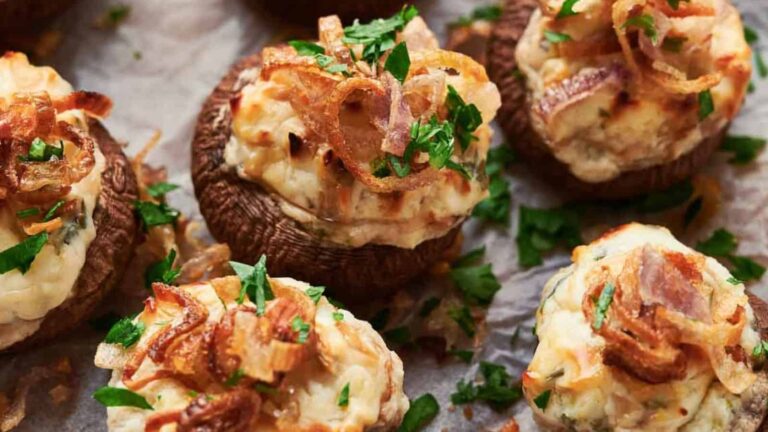 Stuffed mushrooms topped with chopped parsley and crispy fried onions on parchment paper.