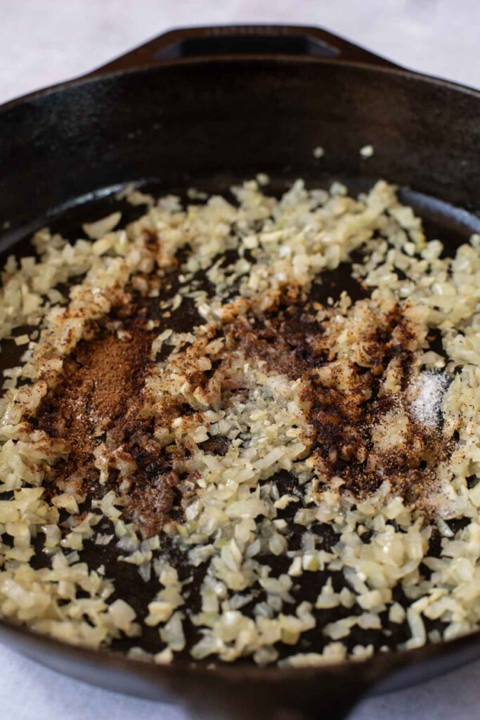 Chopped onions saut&eacute;ing in a cast iron skillet with various ground spices, forming the flavorful base for Sweet Potato and Black Bean Tacos.